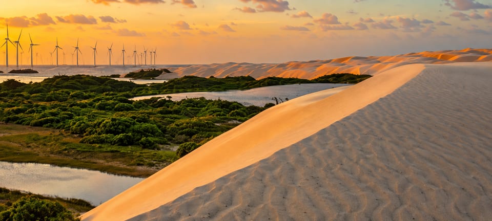 Dunas e lagoas ao pôr do sol, com aerogeradores ao fundo