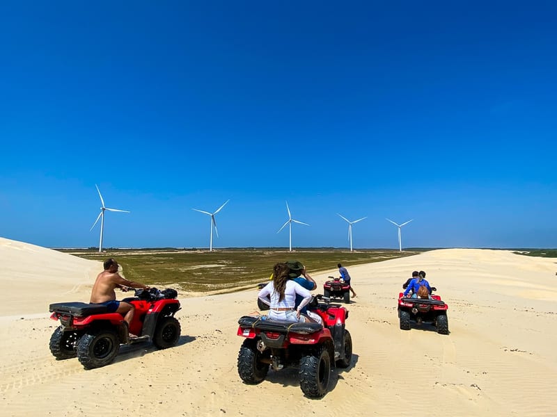 Quadriciclos em passeio pelas dunas, com aerogeradores ao fundo